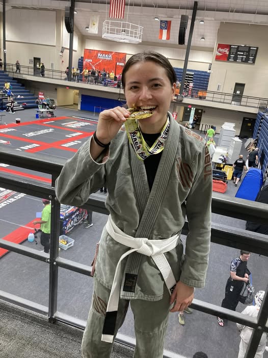 Young female martial artist in gi holding medal at competition.