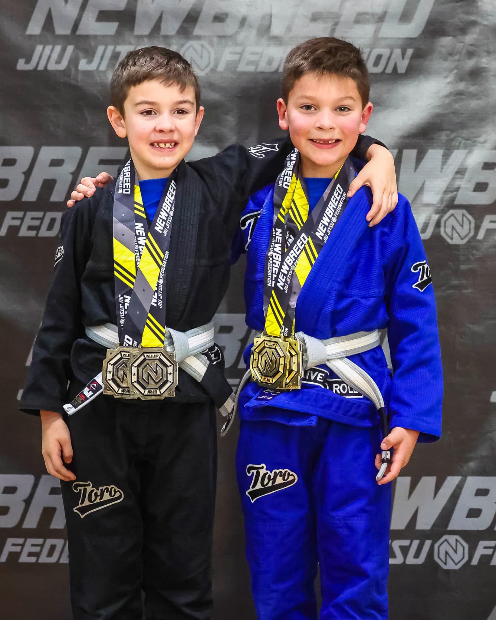 Kids in black and blue BJJ gis smiling with medals after competition at Absolute Jiu-Jitsu Academy.