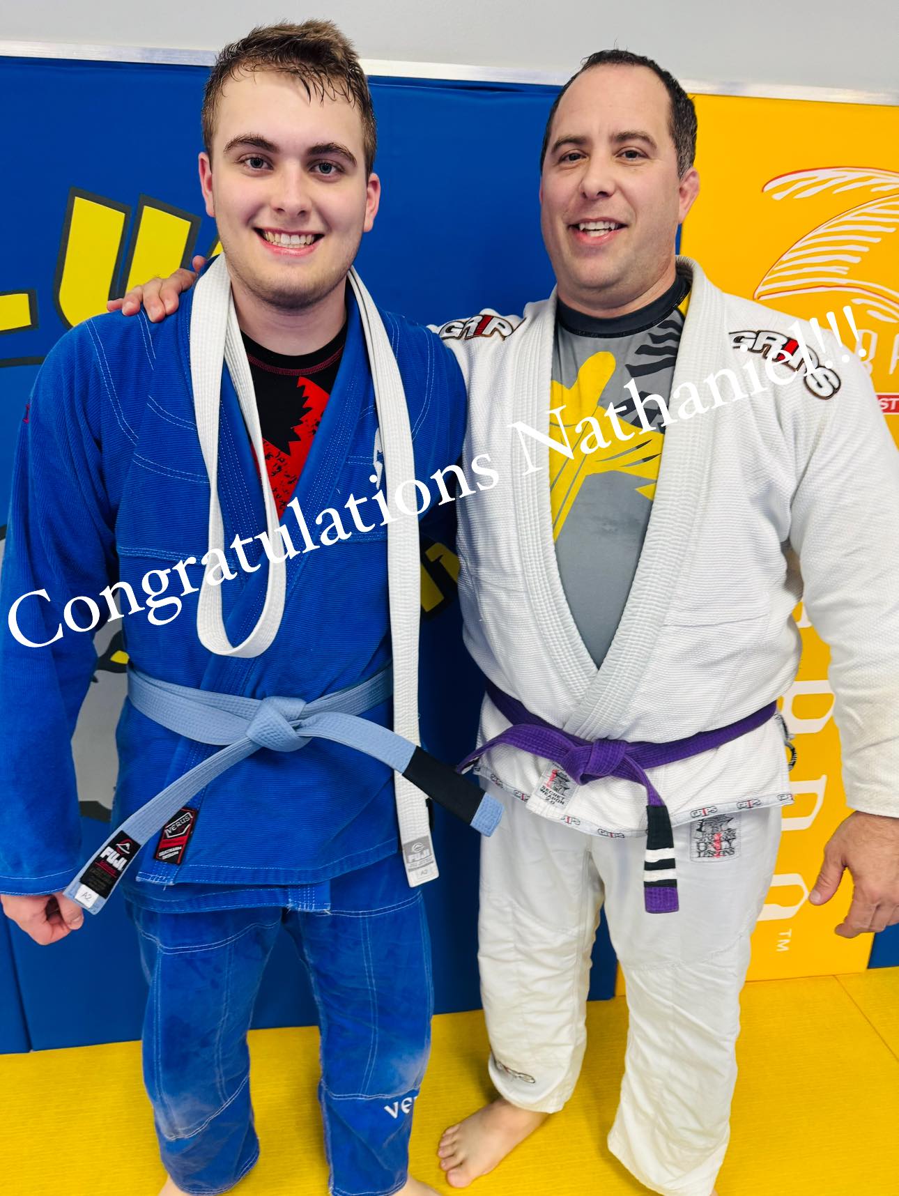 Two practitioners in blue and white gis celebrating their success at Absolute Jiu-Jitsu Academy.