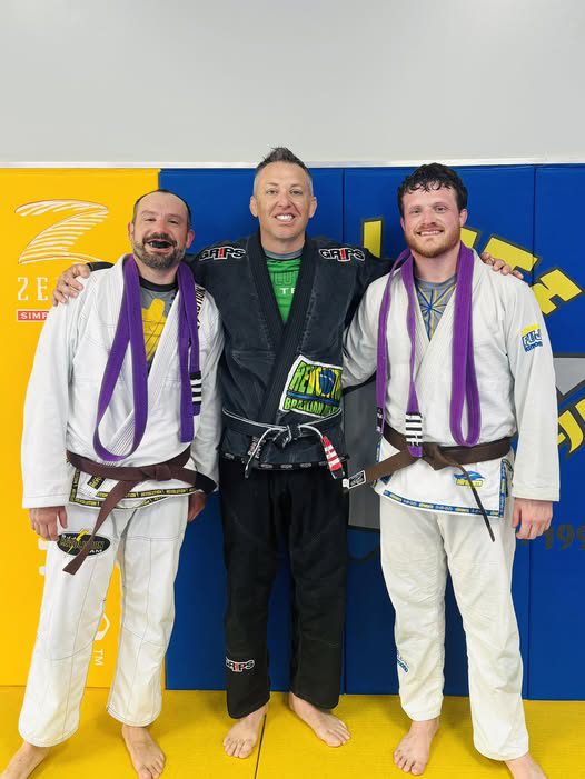 2. Three men in Brazilian Jiu-Jitsu gis celebrating success at Absolute Jiu-Jitsu Academy, wearing purple belts and pose proudly.