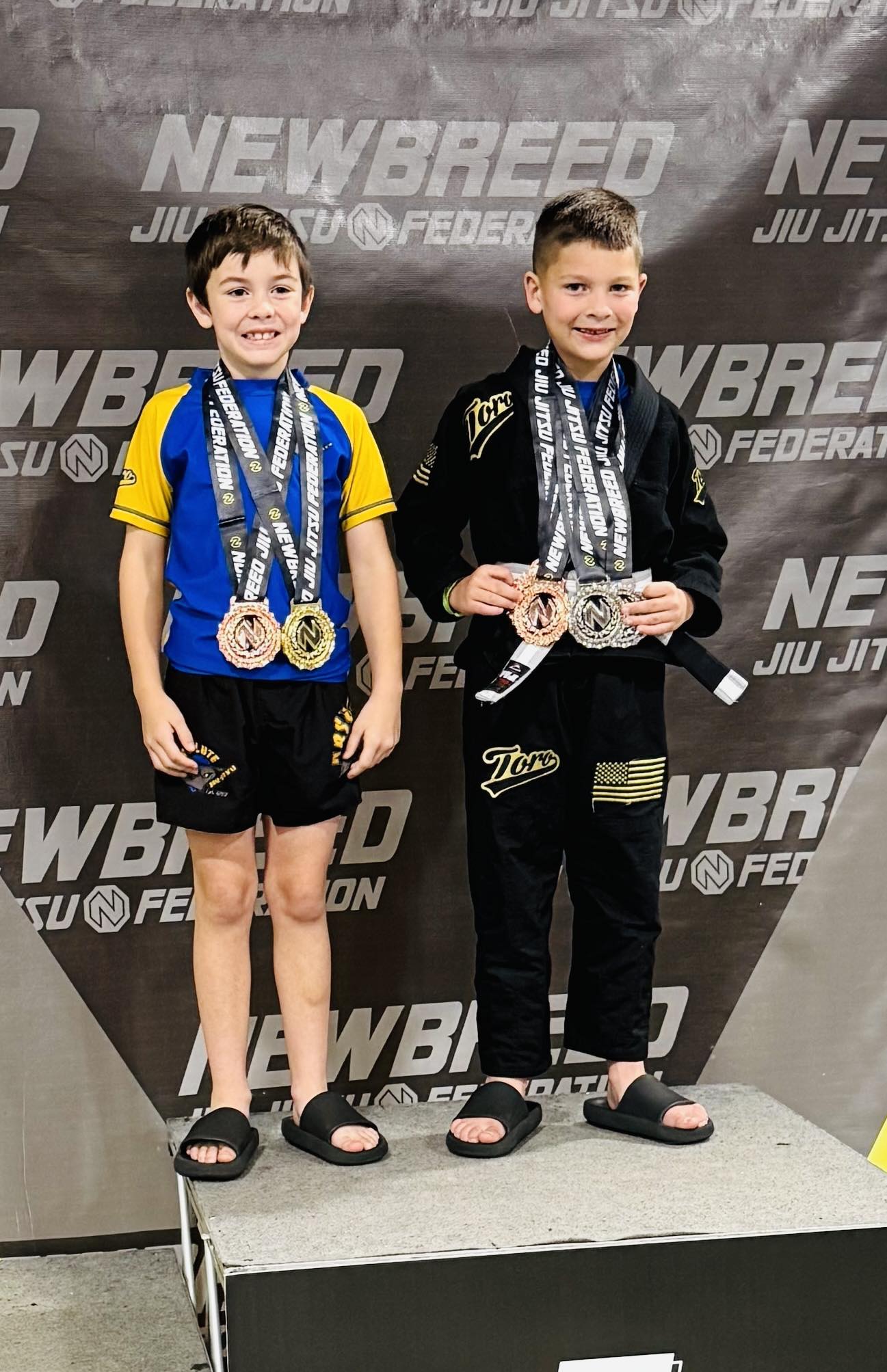 Young martial artists celebrating victory with medals at Absolute Jiu-Jitsu Academy competition.