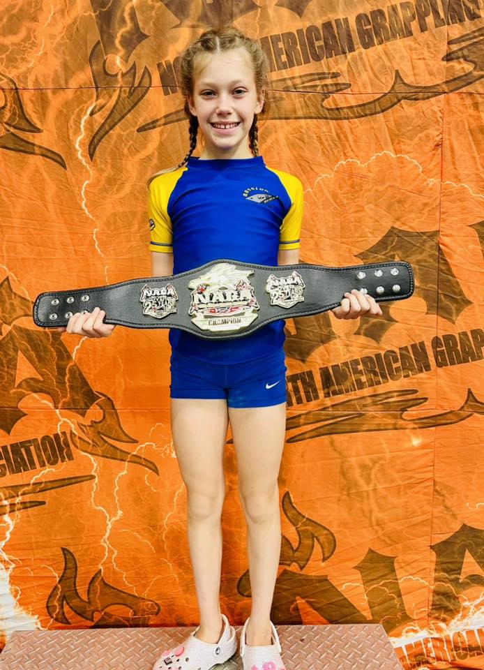 Girl holding BJJ championship belt at Absolute Jiu-Jitsu Academy.