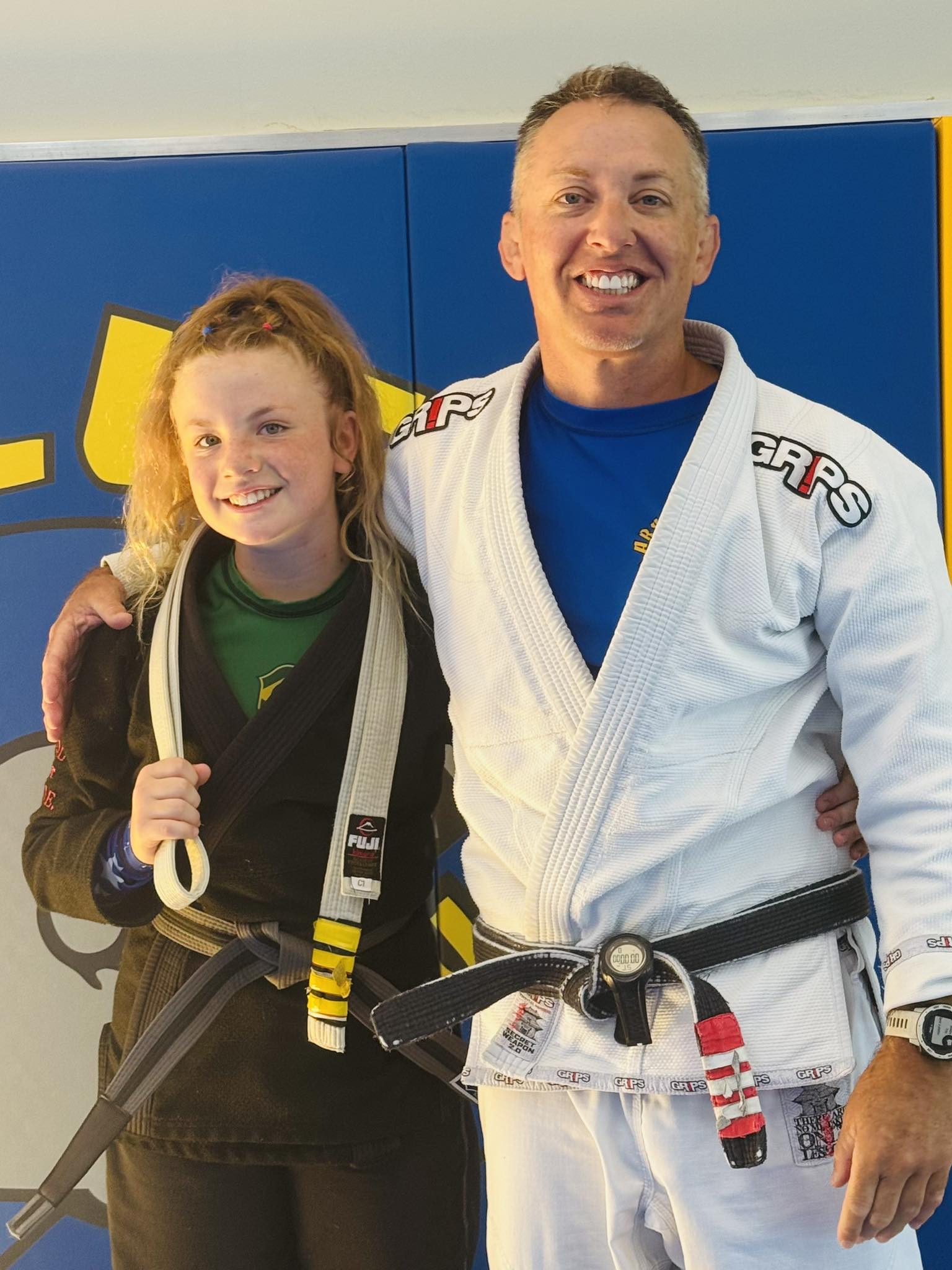 Friendly instructor with young student in Brazilian Jiu-Jitsu gi uniform, smiling after training session.