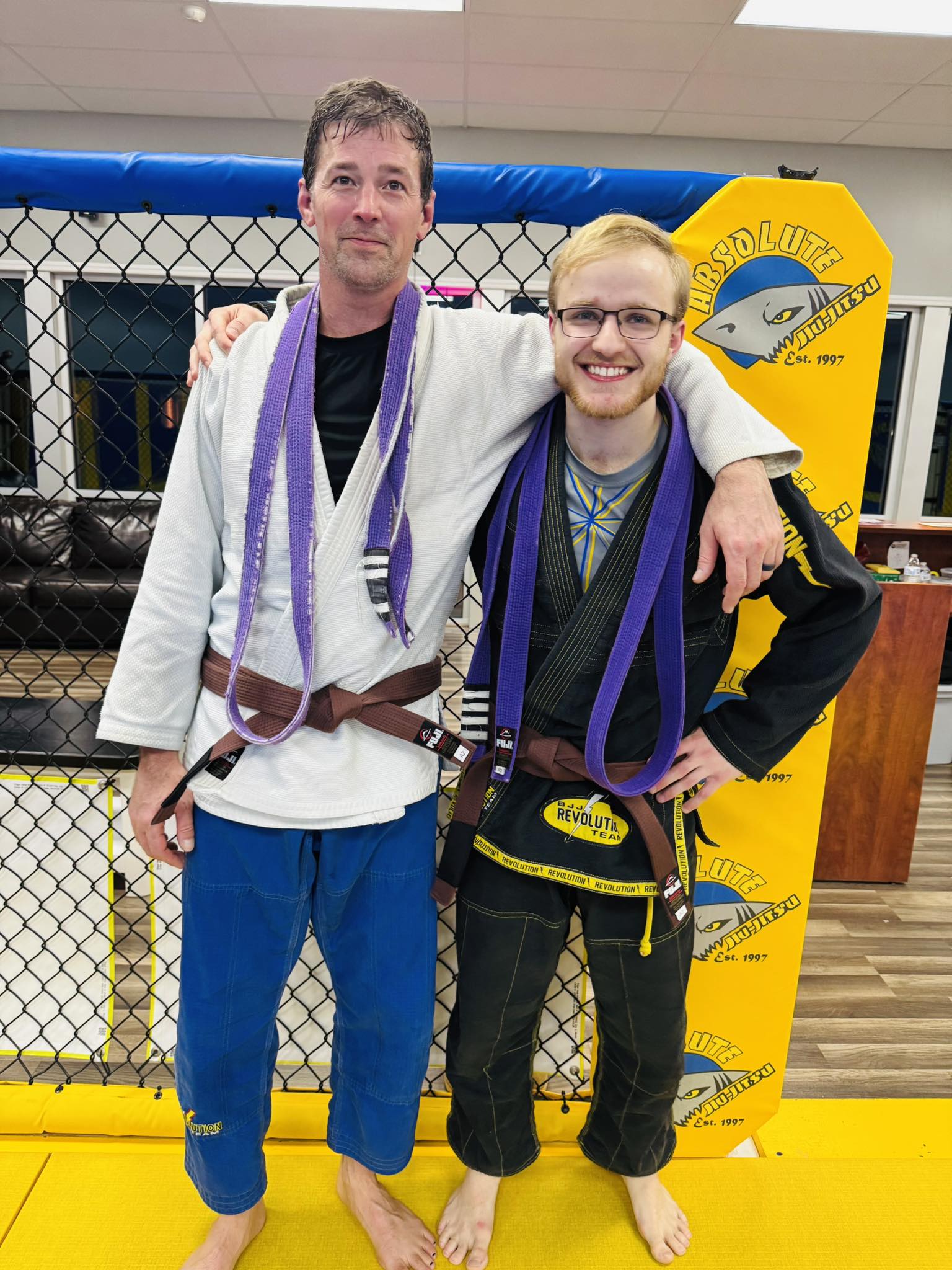Group photo of two male BJJ practitioners with belts after class at Absolute Jiu-Jitsu Academy.